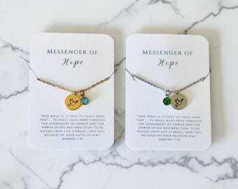 May include: Two necklaces on white display cards. One gold-tone necklace features a round pendant with a dove engraving and a light blue crystal. One silver-tone necklace features a round pendant with a dove engraving and a green crystal.