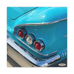 May include: The rear quarter panel of a bright turquoise vintage car featuring three circular taillights with chrome trim. Two outer lights are red, and the centre light is clear. A polished chrome bumper runs along the bottom edge of the vehicle.