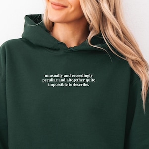May include: A dark green hoodie with a front pocket and a hood. The text "unusually and exceedingly peculiar and altogether quite impossible to describe" is printed on the chest. The word "Forest" is written in cursive at the bottom left.