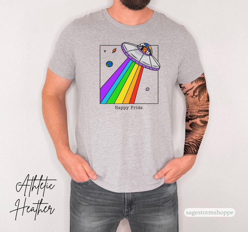 Pu&ograve; includere: T-shirt grigio athletic heather con una grafica colorata di un UFO che emette un arcobaleno. Il design include pianeti e la scritta "Happy Pride". La maglietta &egrave; un capo d'abbigliamento casual.