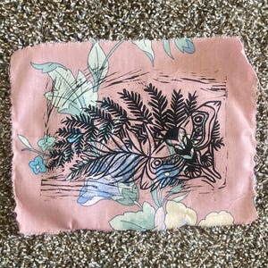 May include: A rectangular piece of pink fabric with a botanical print. The print features black, blue, and white floral and leaf designs. The edges of the fabric are unfinished.