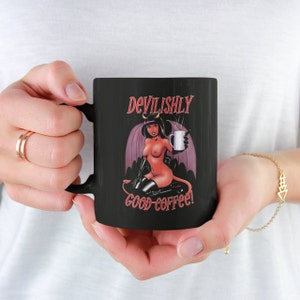 May include: Black coffee mug with a red and black illustration of a devil woman holding a cup of coffee. The text "Devilishly good coffee!" is printed on the mug.