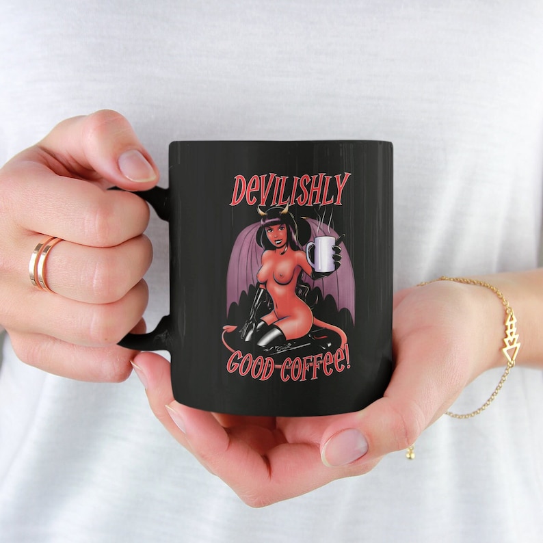 May include: Black coffee mug with a red and black illustration of a devil woman holding a cup of coffee. The text "Devilishly good coffee!" is printed on the mug.