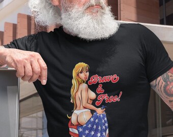 May include: Black t-shirt featuring a pin-up style illustration of a woman partially draped in an American flag. The text "Brave & Free!" is above the illustration in red and white. The shirt is worn by a person with a white beard and sunglasses.