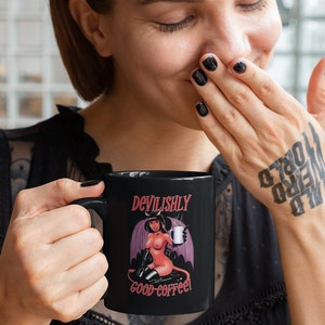 May include: Black coffee mug with a red and black illustration of a woman with devil horns and wings holding a coffee cup. The text on the mug reads "Devilishly good coffee!"