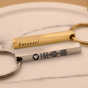 May include: Two metal keychains. One is gold-colored with the word "Forever!" engraved on it. The other is silver-colored with a heart symbol and a music code engraved on it. Both keychains have a ring for attaching keys.