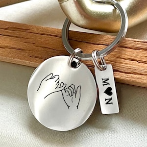 May include: Silver keychain with two linked hands and a small tag that says "N ♥ M".