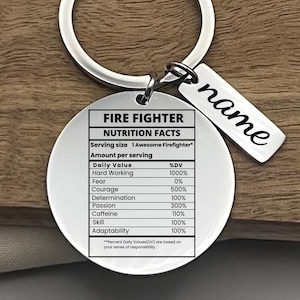 May include: A silver keyring with a round pendant displaying a "Fire Fighter Nutrition Facts" label. The label lists daily values for attributes like hard work, courage, and passion. A smaller rectangular tag with the name "name" is also attached.