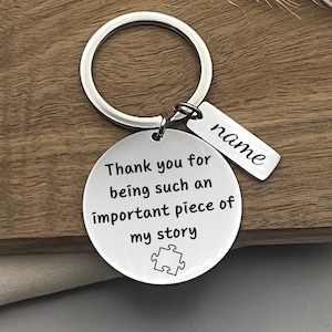 May include: Silver keychain with a round charm that says "Thank you for being such an important piece of my story" with a puzzle piece symbol. A smaller tag is attached to the keychain that says "name".