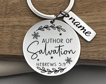 Könnte beinhalten: Ein silberfarbener Schlüsselanhänger mit einem runden Anhänger, auf dem "AUTHOR OF Salvation" und "HEBREWS 5:9" stehen. Ein kleines rechteckiges Etikett mit dem Wort "name" ist ebenfalls angebracht. Das Design umfasst Schneeflocken- und Blätter-Motive.