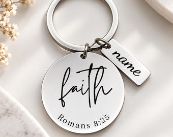 Könnte beinhalten: Ein silberfarbener Metallschlüsselanhänger mit einer runden Scheibe, die mit dem Wort faith und dem Text Romans 8:25 in Schwarz graviert ist. Am Ring befindet sich ein kleinerer rechteckiger Metallanhänger mit dem Wort name in schwarzer Schrift.