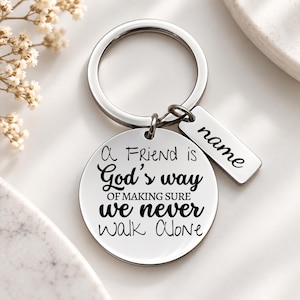 May include: A silver-toned metal keychain featuring a circular pendant engraved with the black text A Friend is God's way OF MAKING SURE we never walk ALONE and a smaller rectangular tag with the word name engraved in black script.