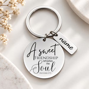 May include: A silver-toned metal keychain featuring a circular pendant engraved with the text A sweet FRIENDSHIP refreshes the Soul PROVERBS 27:9 and a smaller rectangular tag with the word name engraved in a black script font.