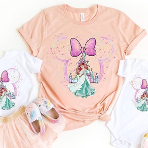 Puede incluir: Un conjunto de dos camisetas blancas con un lazo rosa y una princesa frente a un castillo. La camiseta m&aacute;s grande es de color melocot&oacute;n y la m&aacute;s peque&ntilde;a es un body. Las camisetas est&aacute;n dispuestas sobre un fondo blanco.