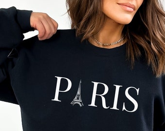 May include: Black sweatshirt with a white graphic of the Eiffel Tower and the word "PARIS" printed on the front.