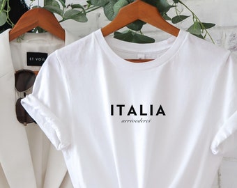 Könnte beinhalten: Weißes T-Shirt mit schwarzem Text, der "ITALIA" und "arrivederci" auf einem Kleiderbügel sagt. Das T-Shirt hängt an einem Gestell mit einem weißen Blazer daneben.