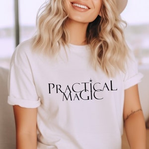 May include: White t-shirt with the text "PRACTICAL MAGIC" in black lettering with a small star above the word "MAGIC".