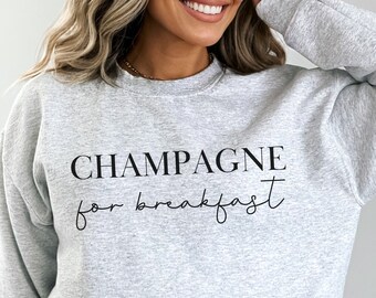 Pode incluir: Camisola cinzenta com o texto "Champagne for breakfast" impresso a preto.