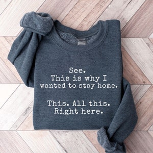 May include: A dark gray sweatshirt with the text "See. This is why I wanted to stay home. This. All this. Right here." printed in white.