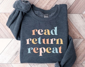 May include: A dark gray sweatshirt with the text "read return repeat" in colorful letters. The letters are in a pastel color scheme of pink, yellow, blue, and orange.