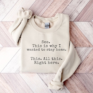 May include: A beige sweatshirt with the text "See. This is why I wanted to stay home. This. All this. Right here." printed in black.