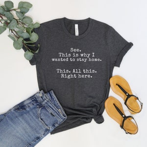 May include: A dark gray t-shirt with white text that reads "See. This is why I wanted to stay home. This. All this. Right here."