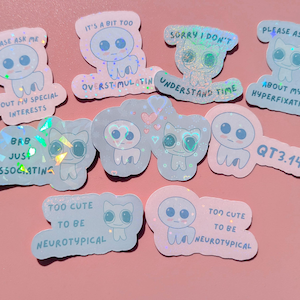 Op de afbeelding: Een verzameling holografische stickers met schattige, cartoonachtige personages en zinnen. De stickers bevatten verschillende ontwerpen, waaronder buitenaardse figuren en katachtige wezens, met tekst als "Vraag me alsjeblieft naar mijn speciale interesses".