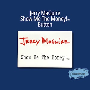 May include: A white rectangular button featuring the text "Jerry Maguire" in red script above "Show Me The Money!" in black. The button is set against a dark blue background, with the text "Jerry Maguire Show Me The Money! Button" at the top.