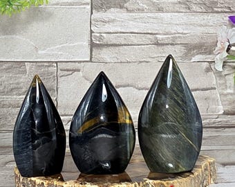 May include: Three teardrop-shaped polished gemstones in shades of blue and green, displayed on a natural wood slice. The gemstones have a glossy finish and varying patterns. The gemstones are labeled A, B, and C.