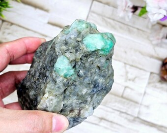 May include: A rough, gray rock with several bright green emerald crystals embedded in it.