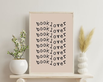 May include: A beige framed print with the word "booklover" repeated seven times in black text on a light peach background.
