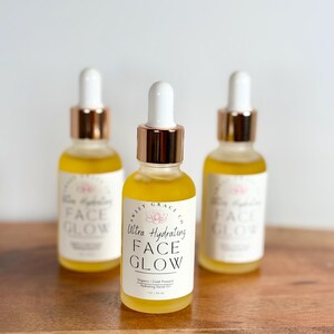 May include: Three amber glass bottles with gold caps and droppers filled with a yellow liquid. The bottles are labelled "Sweet Grace Co. Ultra Hydrating Face Glow. Organic | Cold Pressed Hydrating Facial Oil 1 fl oz / 30 ml."