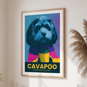 Könnte beinhalten: Ein gerahmter Kunstdruck mit einem stilisierten Porträt eines Cavapoo-Hundes, der einen violett-gelben Strickpullover trägt und einen gelben Kaffeebecher hält. Der Text am unteren Rand lautet CAVAPOO Coffee Shop Companion in Gelb und Weiß.
