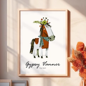 Könnte beinhalten: Ein gerahmter Kunstdruck mit einer stilisierten Illustration eines braun-weißen Pferdes mit Blumenkranz und einem blau gemusterten Schal. Der Text "Gypsy Vanner" und "Free Spirit" ist in Schwarz unter dem Pferd auf weißem Grund gedruckt.