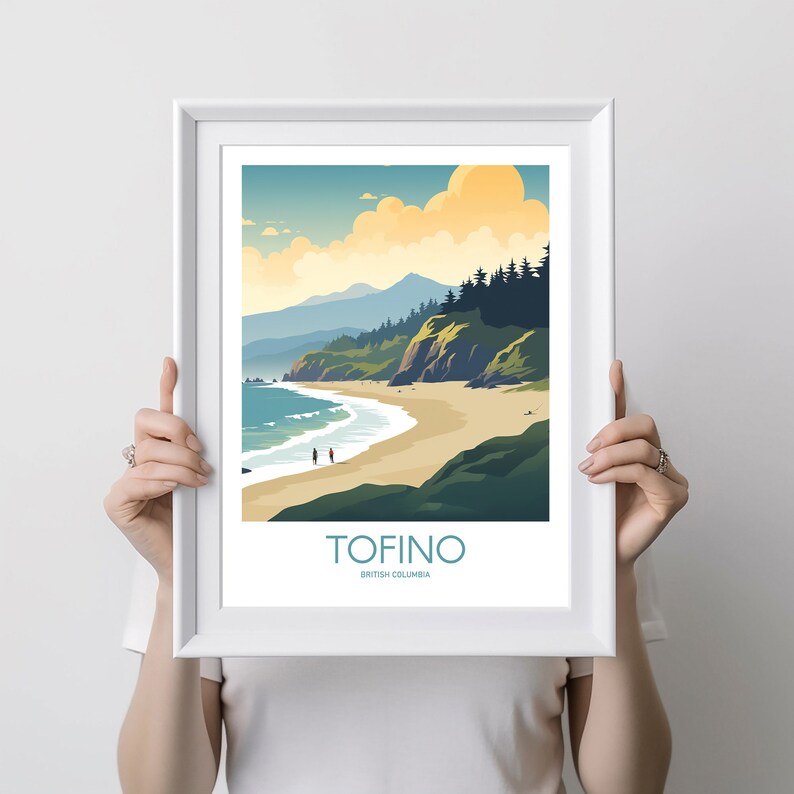 Op de afbeelding: Een ingelijste kunstdruk met een kustlandschap. Het kunstwerk toont een zandstrand, turquoise water en groene kliffen onder een blauwe lucht met wolken. Het woord "TOFINO" is in turquoise gedrukt, met daaronder "British Columbia".