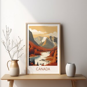May include: A framed art print featuring a stylized landscape of Canada. The artwork depicts a river winding through a valley with mountains in the background. The color palette includes shades of orange, brown, and gray. The word "CANADA" is printed at the bottom.
