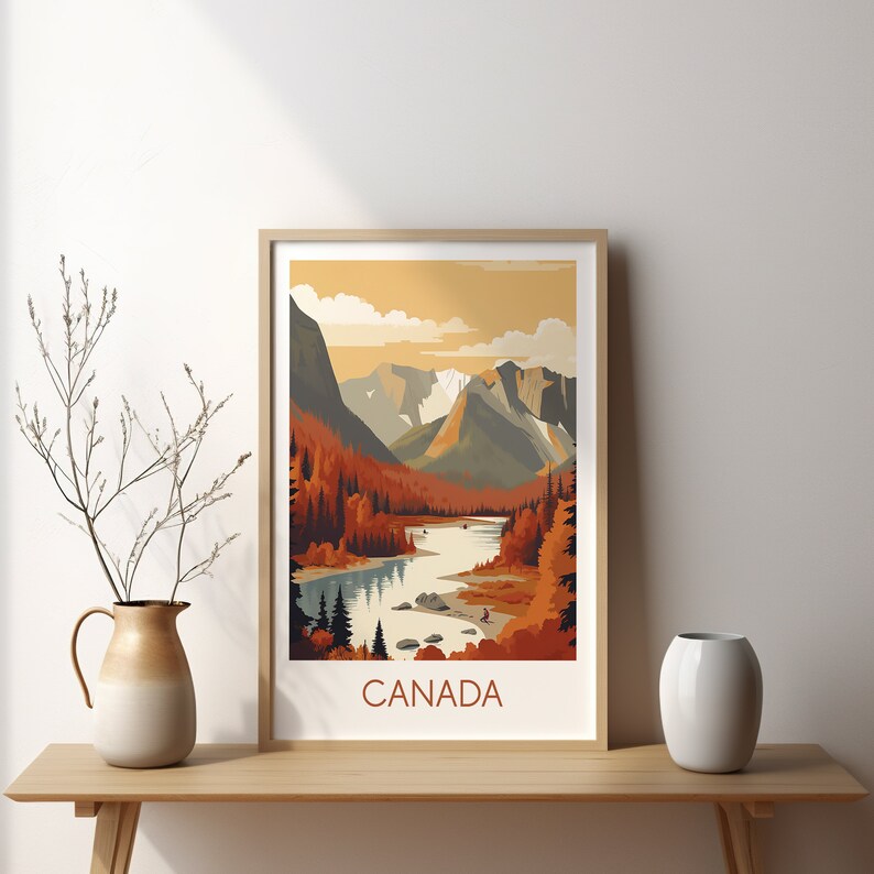 May include: A framed art print featuring a stylized landscape of Canada. The artwork depicts a river winding through a valley with mountains in the background. The color palette includes shades of orange, brown, and gray. The word "CANADA" is printed at the bottom.