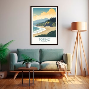 Op de afbeelding: Een ingelijste kunstprint met een kustlandschap met de tekst "TOFINO BRITISH COLUMBIA". Het kunstwerk toont een strand, oceaan, bergen en een ondergaande zon in tinten blauw, groen en geel. Twee figuren lopen op het strand.