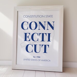 Könnte beinhalten: Ein gerahmter Druck mit dem Wort "CONNECTICUT" in kräftigen blauen Buchstaben, mit dem Text "Constitution State" darüber und "United States of America" darunter. Der Druck enthält das Jahr "Est. 1788" und eine subtile Umrisslinie des Staates.