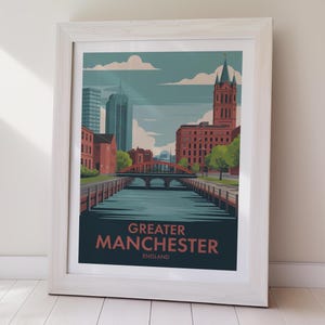 May include: Framed art print featuring a stylized illustration of Greater Manchester, England. The artwork depicts a canal with a red bridge, buildings, and the text "Greater Manchester England" in a dark teal color.