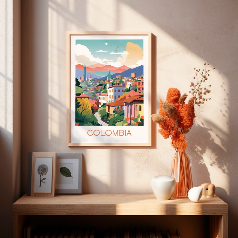 May include: A framed art print featuring a colorful illustration of a cityscape with the word "COLOMBIA" at the bottom. The artwork depicts buildings, mountains, and trees in a stylized manner. The frame is light-colored.