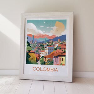 May include: A framed art print featuring a stylized illustration of a Colombian cityscape. The artwork showcases colorful buildings with red tile roofs, set against a backdrop of mountains and a blue sky. The word "COLOMBIA" is printed in orange.