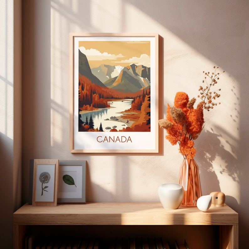 May include: A framed art print featuring a stylized landscape of Canada. The artwork depicts a river winding through a valley with mountains in the background, rendered in warm autumnal colors. The word "CANADA" is printed at the bottom.