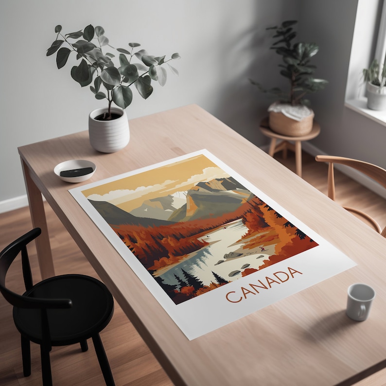 May include: A landscape art print featuring a scenic view of Canada. The print showcases a river winding through a valley, with mountains in the background. The color palette includes shades of orange, brown, and blue. The word "CANADA" is printed in a brown font.
