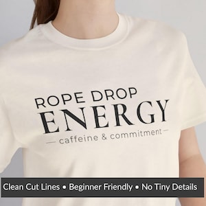 Może przedstawiać: Kremowa koszulka z napisem "ROPE DROP ENERGY" pogrubionymi czarnymi literami. Pod słowem "ENERGY" znajduje się fraza "- caffeine & commitment-". Na dole koszulki znajduje się tekst "Clean Cut Lines • Beginner Friendly • No Tiny Details".