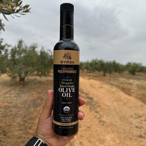 May include: A tall, dark glass bottle of Byrsa organic extra virgin olive oil with a black cap. The label features the text Ultra High Polyphenols, Premium Organic Extra Virgin Olive Oil, Robust Flavor, USDA Organic, Product of Tunisia, and 500 ml.