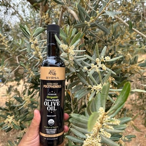 May include: A tall, dark glass bottle of Byrsa organic extra virgin olive oil with a black cap. The label features the text Ultra High Polyphenols, Premium Organic Extra Virgin Olive Oil, Robust Flavor, USDA Organic, and 16.91 fl oz (500 ml).
