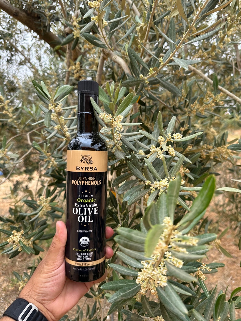 May include: A tall, dark glass bottle of Byrsa organic extra virgin olive oil with a black cap. The label features the text Ultra High Polyphenols, Premium Organic Extra Virgin Olive Oil, Robust Flavor, USDA Organic, and 16.91 fl oz (500 ml).