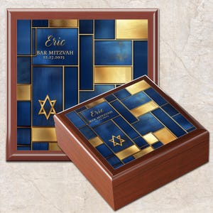 May include: A wooden box and a framed plaque with a blue and gold geometric design. The text "Eric BAR MITZVAH 12.27.2025" is displayed on both items. A Star of David is also featured.