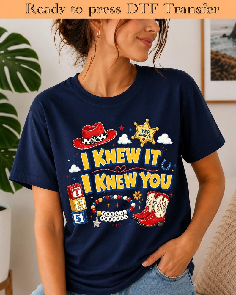 May include: A navy blue short-sleeve t-shirt featuring a graphic print with a red cowboy hat, a yellow sheriff badge with the text YEP, KNEW IT, red cowboy boots, alphabet blocks labeled T, S, 5, and a beaded bracelet with the text YOU & I FOREVER.